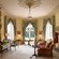 The interior of a room containing a fireplace, large mirrors, antiques, upholstered chairs, a couch, tables and books